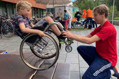 Toine Klerks van Stichting BEN begeleidt een kind in een rolstoel op een rolstoelvaardigheidsparcours.